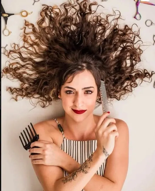 Amanda, cabeleireira e dona do estúdio, com os cachos soltos e um pente garfo na mão